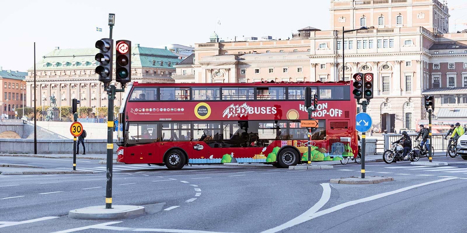 HOHO bus in Stockholm passing a big building with traffic lights on the front and stallgatan sign