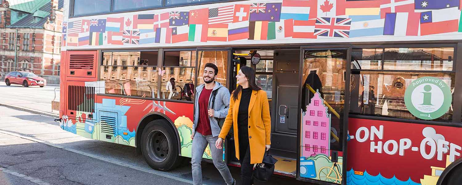 Man and a woman walking out of the HOHO bus, which is decorated with flags,  in Copenhagen