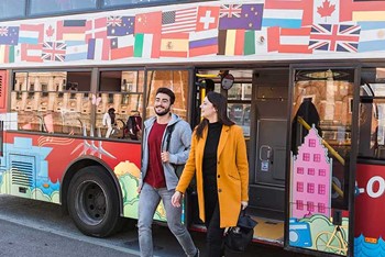 Man and a woman walking out of the HOHO bus, which is decorated with flags,  in Copenhagen